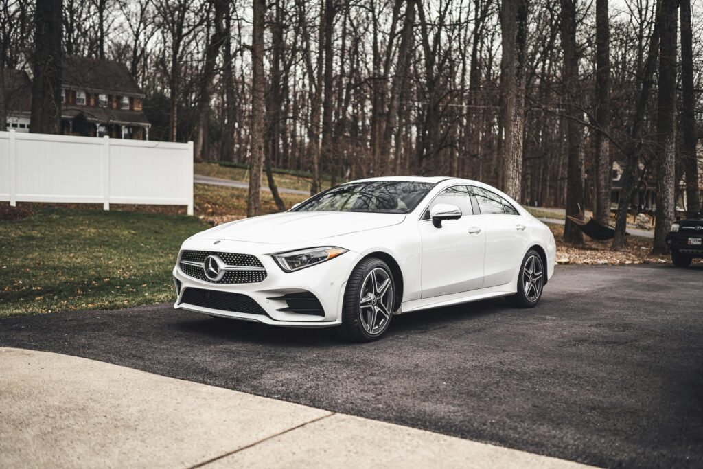 A sleek white Mercedes-Benz sedan parked on a driveway surrounded by a wooded area.